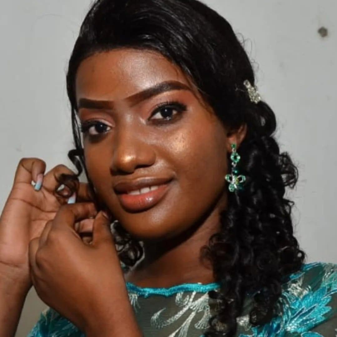 Mulher negra elegante com cabelos cacheados e brincos verdes, sorrindo suavemente para a câmera.